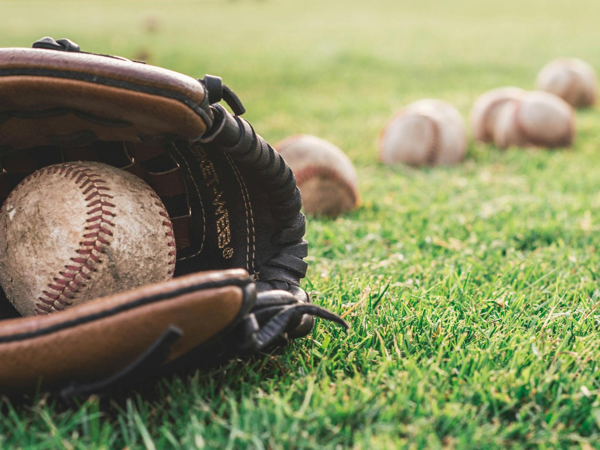 A close-up of a baseball glove with balls on a green field, symbolizing outdoor sports.